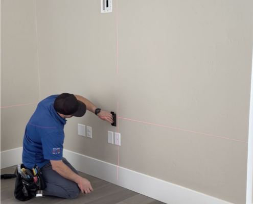 Technician using a laser level to precisely position wall outlets and mounting points for a home media installation.