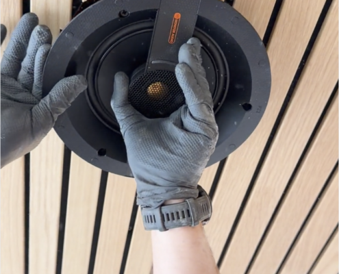 Close-up of a Monitor Audio in-ceiling speaker being installed into a custom wood slat ceiling for whole-home audio.